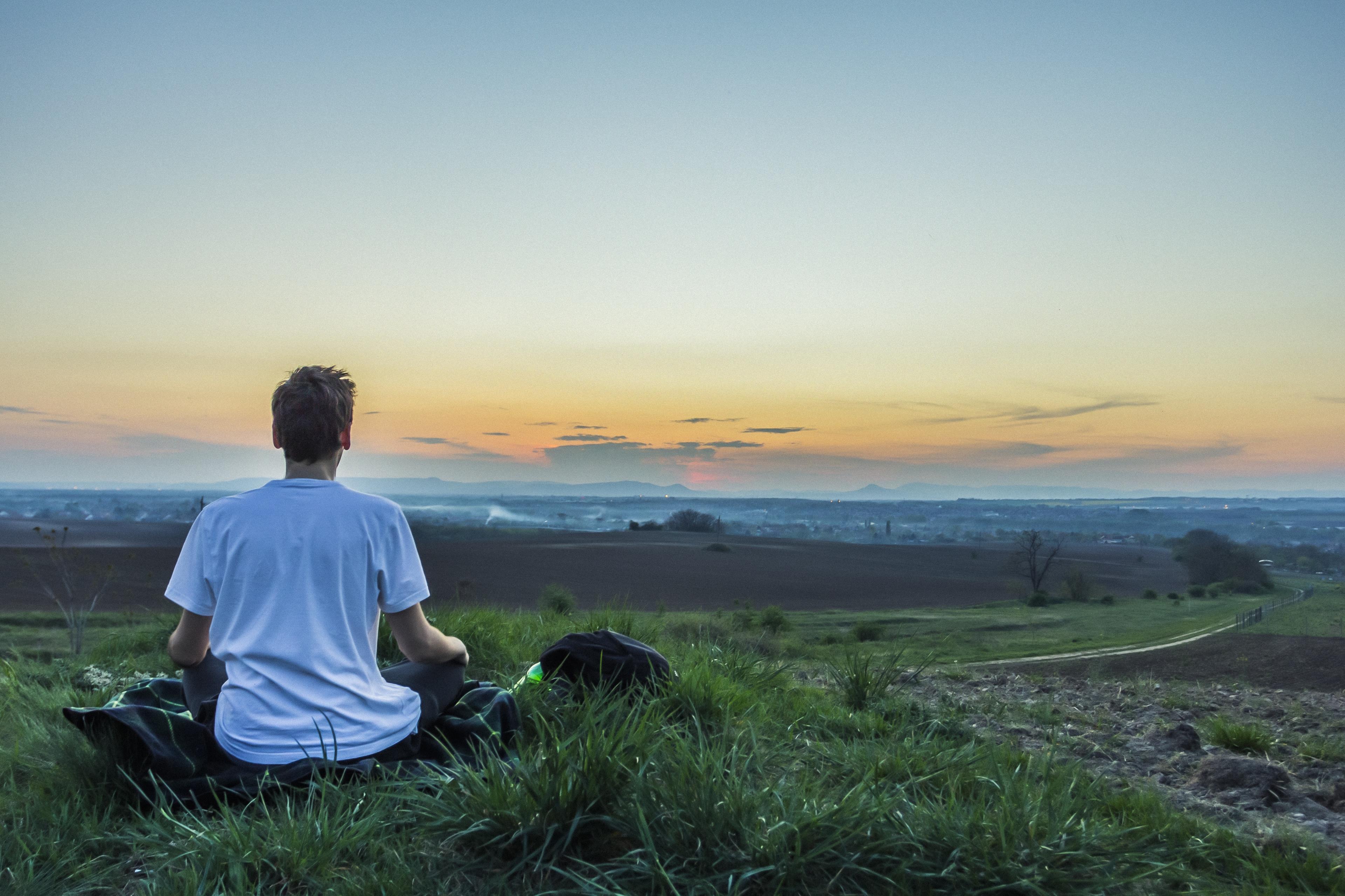 Ragazzo seduto in un prato in posizione meditativa