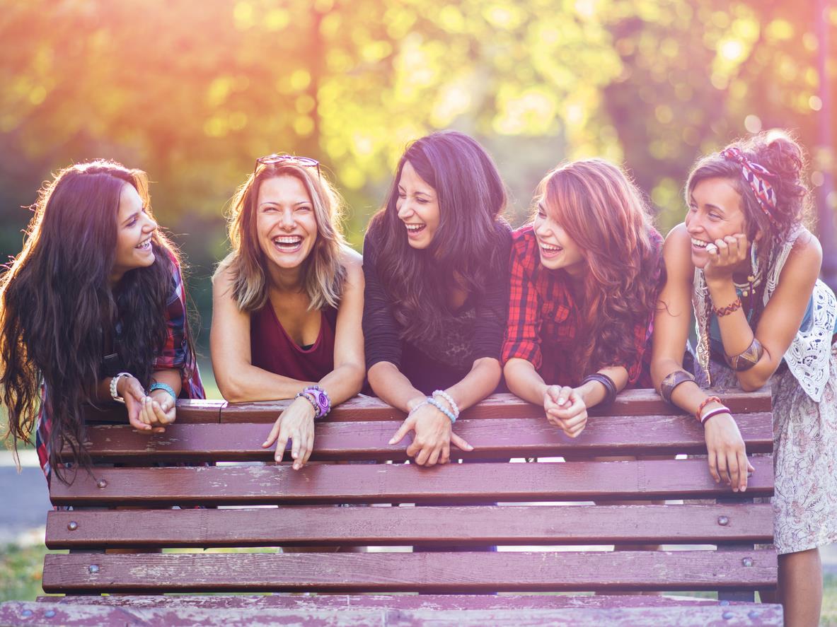 Gruppo di amiche sorride dietro una panchina