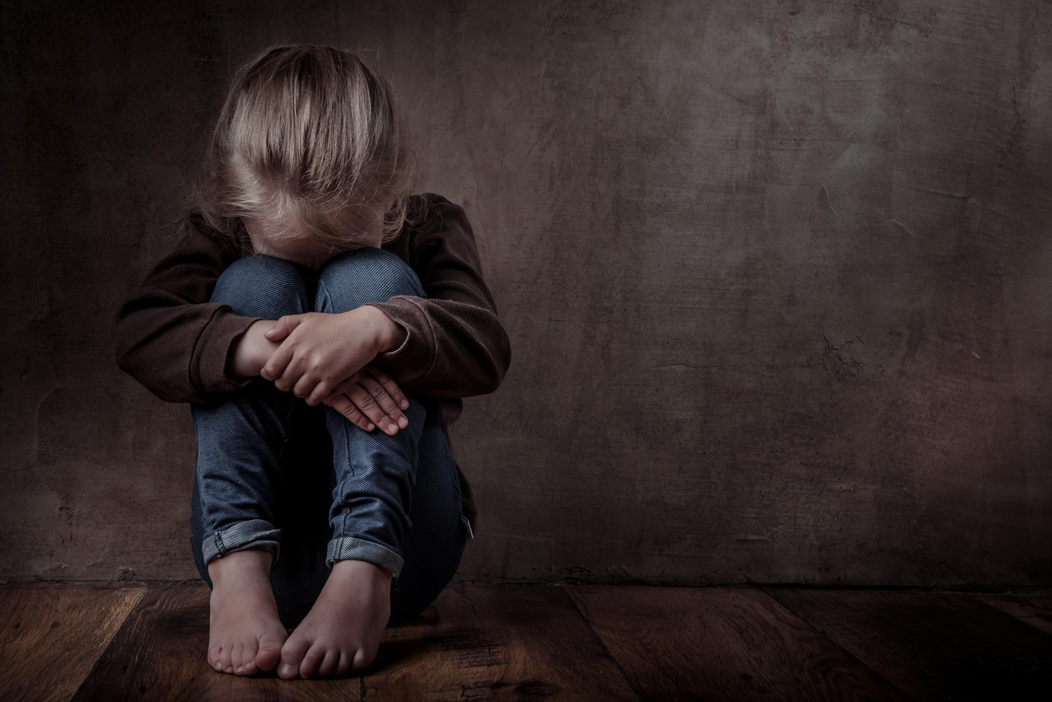 Bambina seduta a terra con le gambe al petto e la testa chinata su di esse