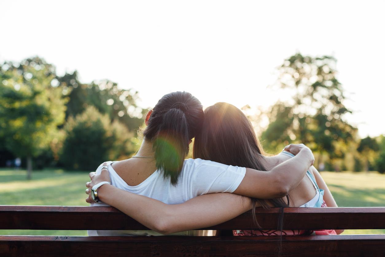 Due amiche sedute su una panchina abbracciate