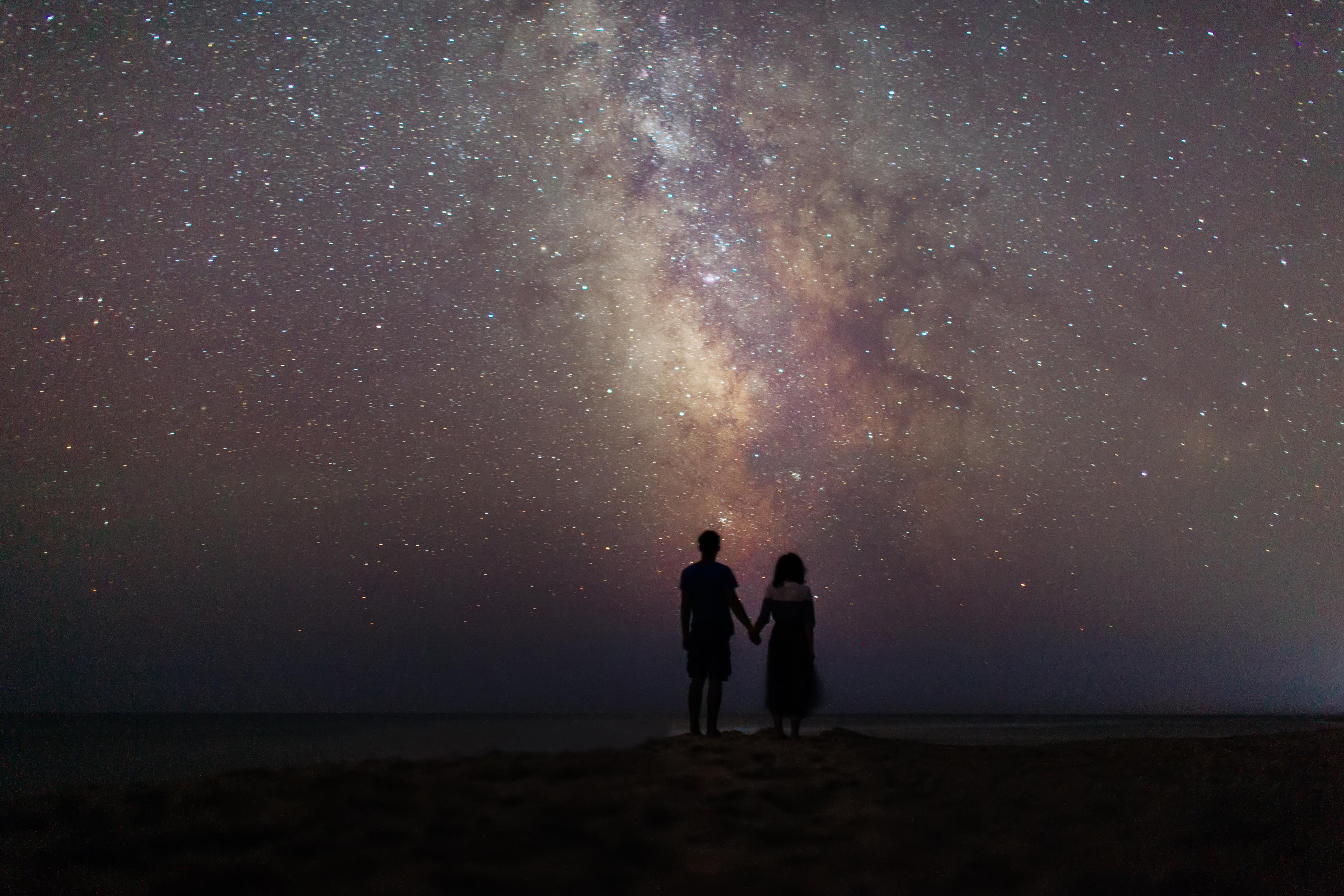 Ragazzo e ragazza si tengono per mano sotto un cielo pieno di stelle