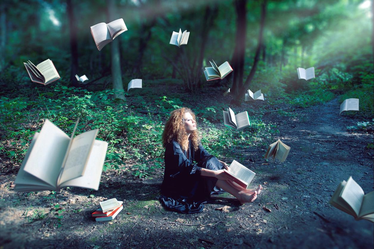 Donna seduta in un bosco circondata dai libri