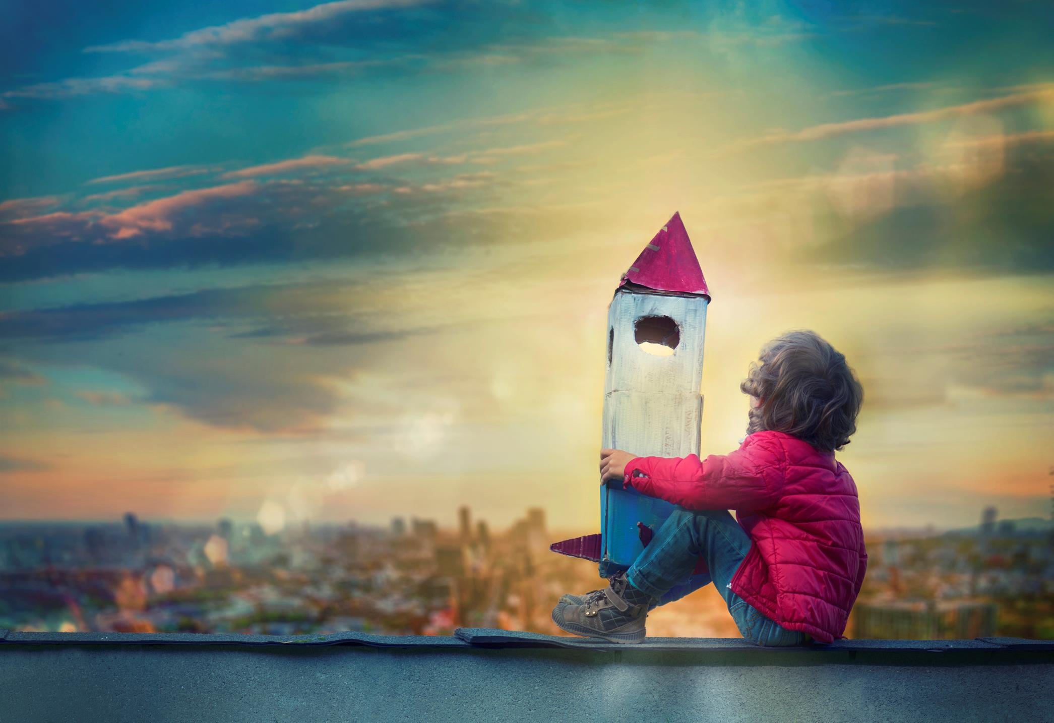 Bambino guarda il cielo con un razzo di cartone