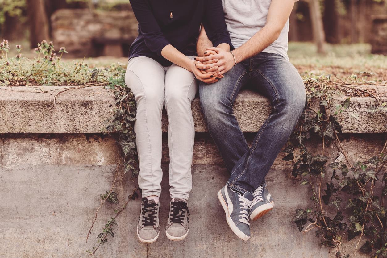 Un ragazzo e una ragazza si tengono per mano seduti su un muretto