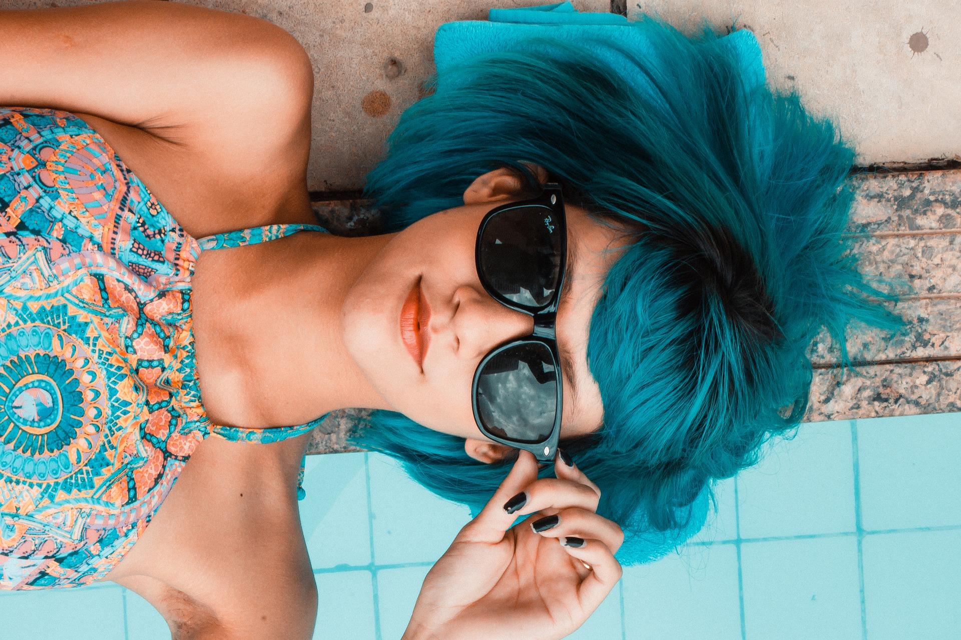 Ragazza sdraiata a bordo piscina con gli occhiali da sole