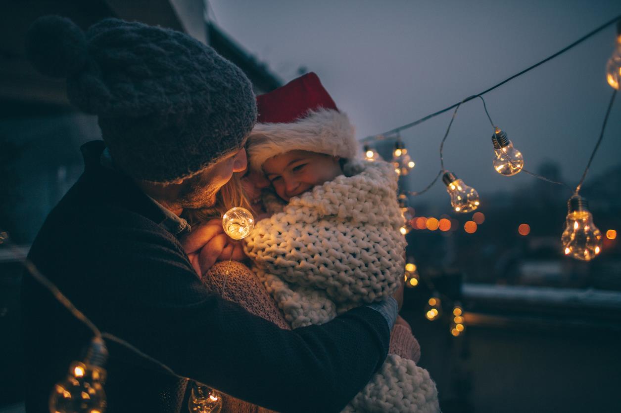 Un padre tiene in braccio la figlia tra le luci natalizie